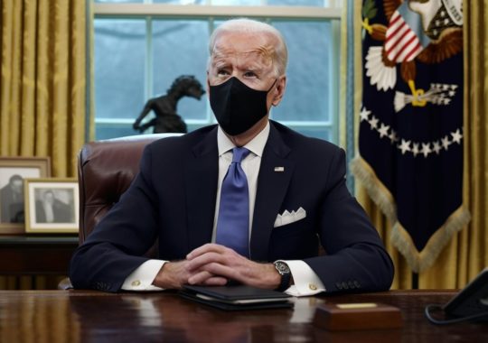 El presidente Biden, con mascarilla, sentado en el Despacho Oval, representado de manera fotorrealista y con tonos púrpuras y ámbar que evocan la conciencia medioambiental.