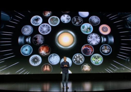 "Presentación de Apple Watches en un escenario, destacados por círculos multicolores de imágenes que recuerdan a nebulosas interestelares, con un estilo que recuerda al director Zack Snyder y una atención detallada a la anatomía, en tonos naranjas claros y blancos, evocando diagramas científicos e imágenes de películas médicas, al estilo del artista Jon McNaught."