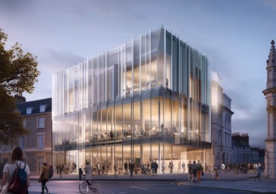 La nueva edificación de la Universidad de Oxford presenta una imponente fachada de vidrio, inspirada en el teatro Kabuki, con una iluminación atmosférica y un movimiento animado, en tonos plateados y beige, evocando el estilo de los artistas Fernand Khnopff, Danh Võ y Gediminas Pranckevicius.