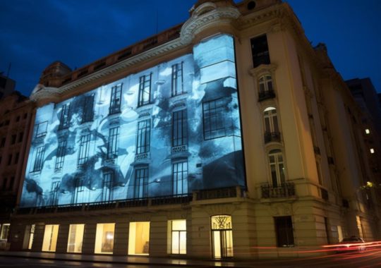 "Una imagen proyectada en un edificio de la ciudad, capturada con una exposición prolongada, que evoca el estilo tradicional y repetitivo de Camille Vivier, Cildo Meireles y Georg Jensen, creando una atmósfera rica e inmersiva."