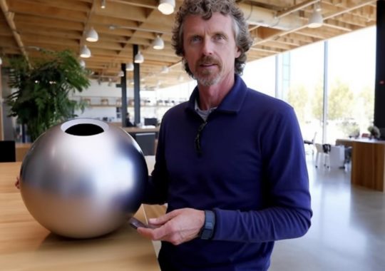 Un hombre parado junto a una esfera plateada, en un ambiente de autenticidad sin pulir y estética futurista.